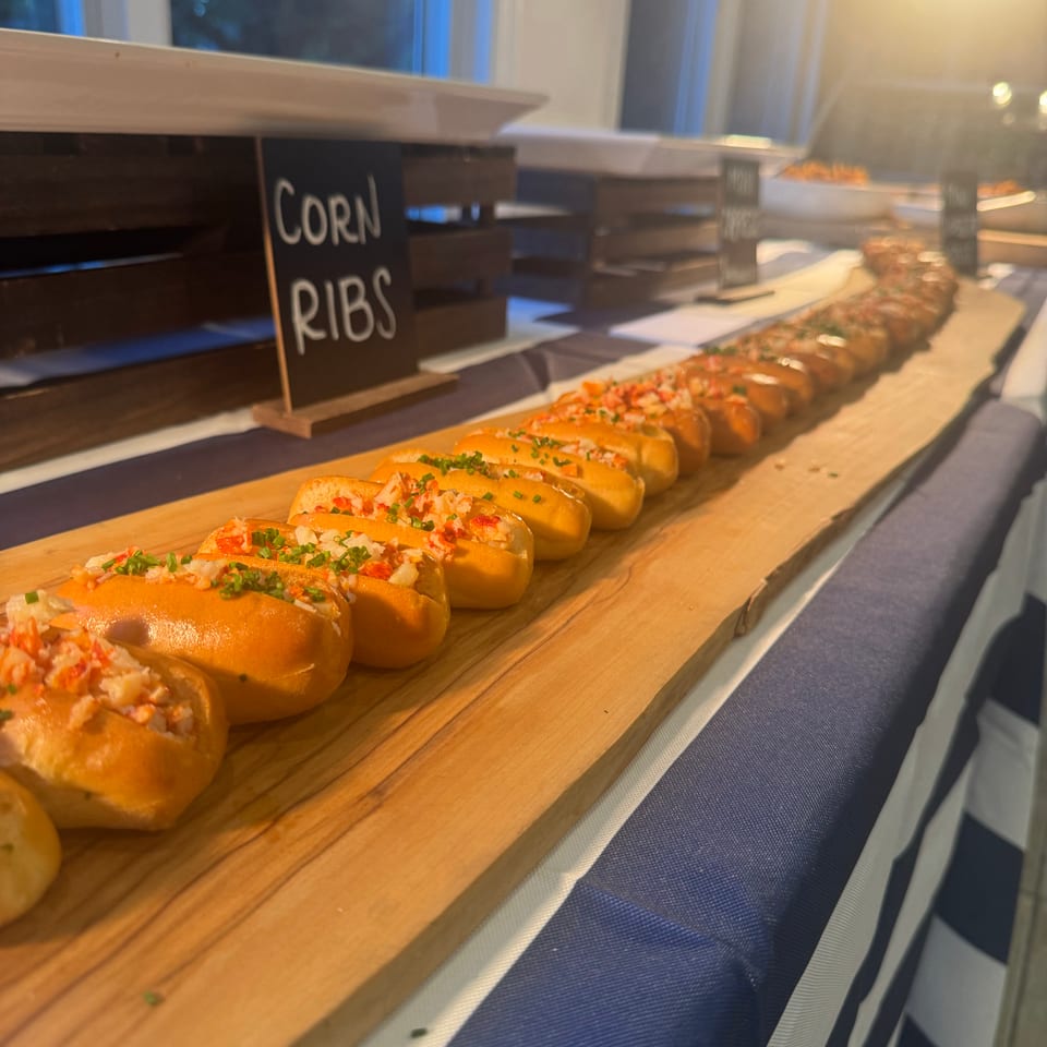 Tray of corn ribs topped with chopped vegetables and herbs displayed on a wooden buffet board.