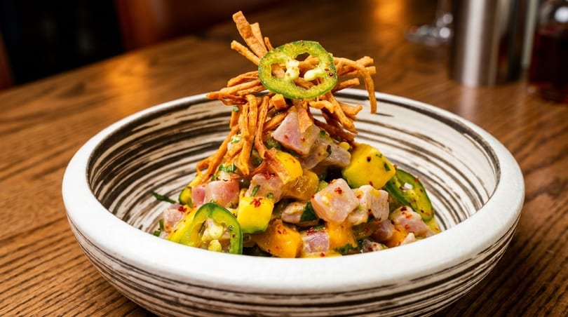 A colorful poke bowl with tuna, mango, jalapeños, and crispy toppings in a decorative bowl.